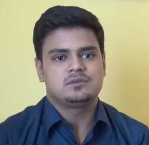 A young man with short, dark hair and a faint beard is wearing a dark blue shirt. He is looking slightly off-camera with a neutral expression, positioned against a plain, yellow background. This image was captured during the NEN seminar organized by the Wadhwani Foundation.