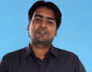 A person with dark hair, wearing a dark shirt, stands against a plain blue background, embodying the professional spirit of Vaibhav Jain from the Wadhwani Foundation.