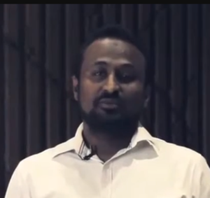 A man with short hair and a beard is speaking in front of a dark, blurred background while wearing a white collared shirt, discussing innovative strategies from Growth Tools.