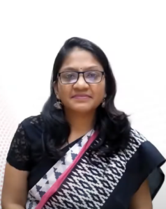 Arpita Sarda, with long dark hair and glasses, is wearing a black and white saree with a pink border. She is sporting dangling earrings and smiling slightly. The background is plain and white, reflecting her poised readiness to venture forward with the InFED-NEN IGNITE Program.