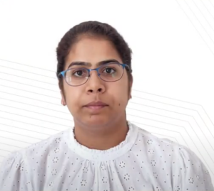 A person with dark hair pulled back, wearing blue-rimmed glasses and a white button-up blouse with a subtle pattern. The background is white with faint diagonal lines, reminiscent of a professional setting where one might be pitching to investors at the NEN IGNITE Program. The expression appears neutral.