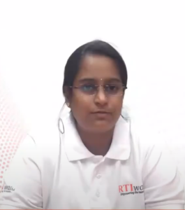 A person with dark hair and glasses, identified as Kritika Mahendra, is wearing a white polo shirt with the logo "RTI wala" on it. The background is plain white with a subtle pattern on the left side. Kritika, a participant in the InFED-NEN IGNITE Program, appears to be looking slightly towards the camera.