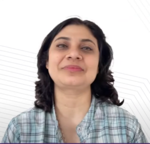 A woman with shoulder-length dark hair is smiling softly. She is wearing a plaid shirt with shades of gray and green. The background, designed for the NEN IGNITE Program, features white diagonal lines creating a minimalistic pattern.