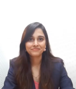 A woman with long dark hair wearing a dark blazer and a peach top is seated against a plain white background. She has a slight smile on her face and is looking directly at the camera, embodying the confidence fostered by the IGNITE Program's customized support.