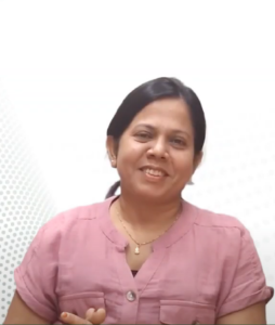 Sangita Singh, with dark hair tied back, is smiling at the camera. She is wearing a short-sleeved pink blouse and a small pendant necklace. The background is light with a subtle dotted pattern on the left side. She recently participated in the InFED-NEN IGNITE Program to learn how to pitch effectively.