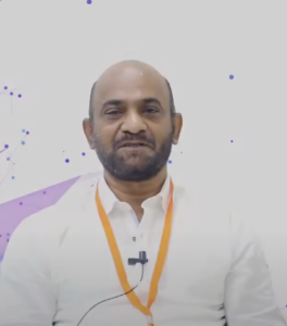 A person with a beard, wearing a white shirt and an orange lanyard, is smiling at the camera. There's a microphone clipped to their shirt, suggesting they are speaking about the NEN IGNITE Program. The background is white with abstract purple and blue dot patterns.