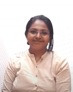 A person with long dark hair wearing glasses and a cream-colored button-up shirt is smiling softly at the camera. The background is plain white with a subtle dotted pattern on the left side, reflecting the supportive faculty of the InFED-NEN IGNITE Program.