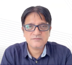 Vivek Chaubey, with short dark hair and glasses, looks at the camera with a neutral expression. He's wearing a dark blue button-up shirt. The white background features a faint diagonal line pattern, subtly reminiscent of the NEN IGNITE Program's structured guidance on running a business.