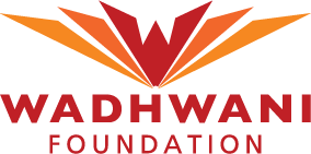 La imagen parece ser un logotipo compuesto por alas estilizadas o formas abstractas que forman una "w" sobre el texto "fundación wadhwani". La combinación de colores incluye tonos naranja y verde sobre