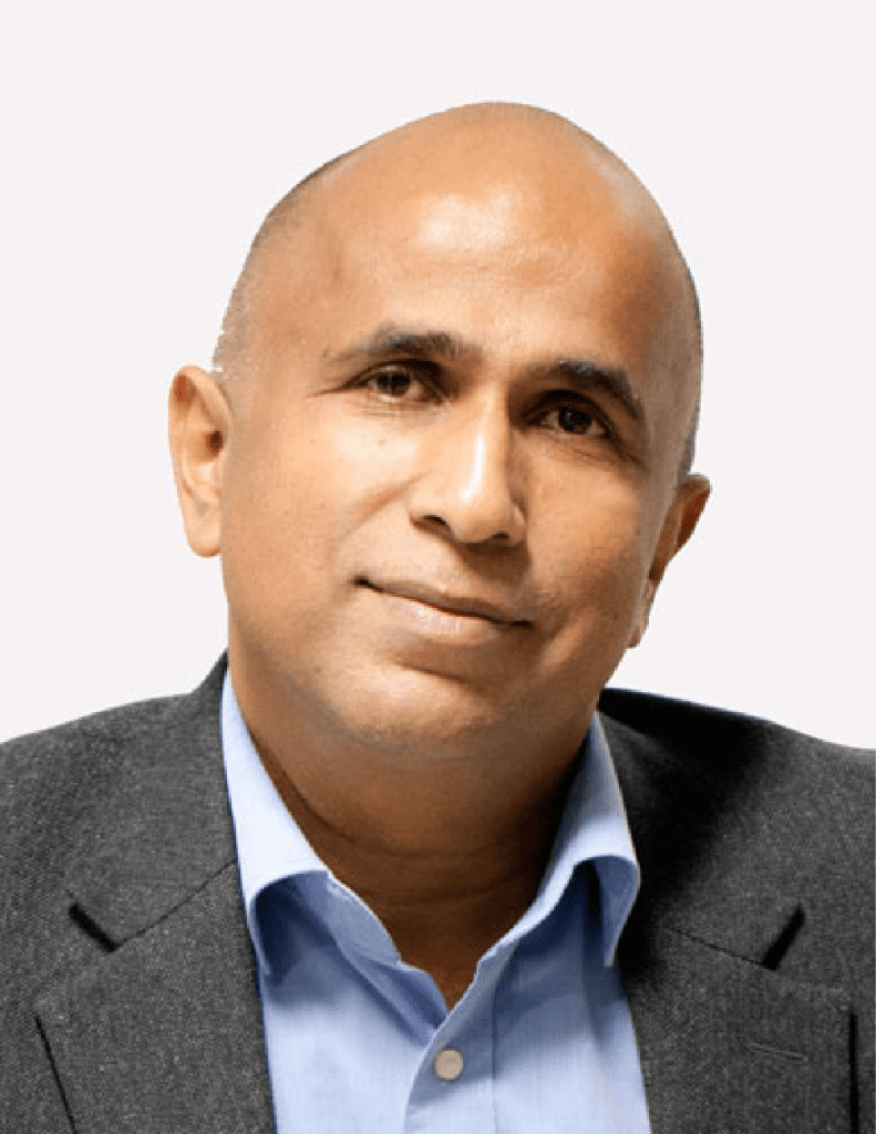 Retrato de Ganesh Krishnan, um homem careca com expressão confiante e acessível, vestindo camisa azul e blazer escuro em um fundo claro.