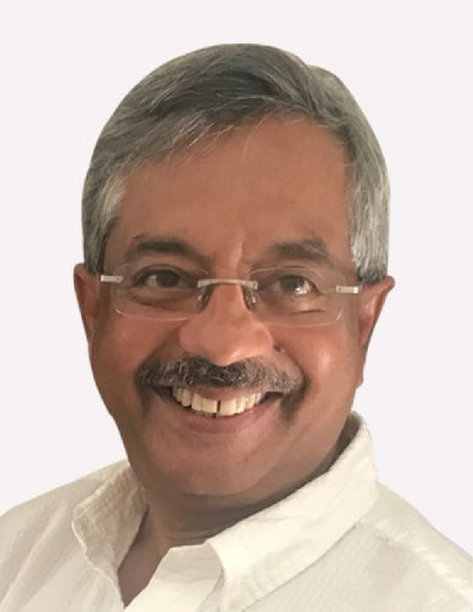 Um senhor alegre, Pramod Bhasin, com óculos e bigode, vestindo uma camisa branca, em um fundo liso.