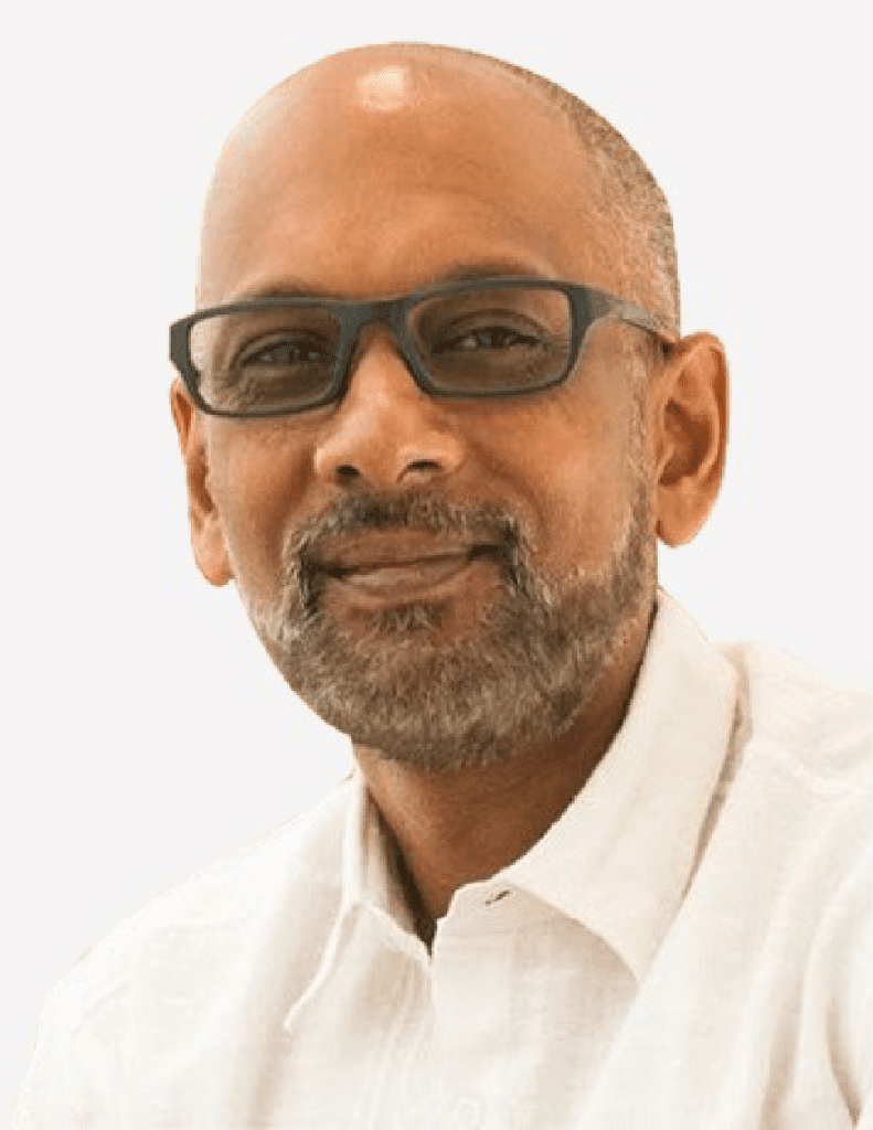 A confident Raghu Mallena, a middle-aged man with glasses and a bald head, wearing a white shirt against a light background.