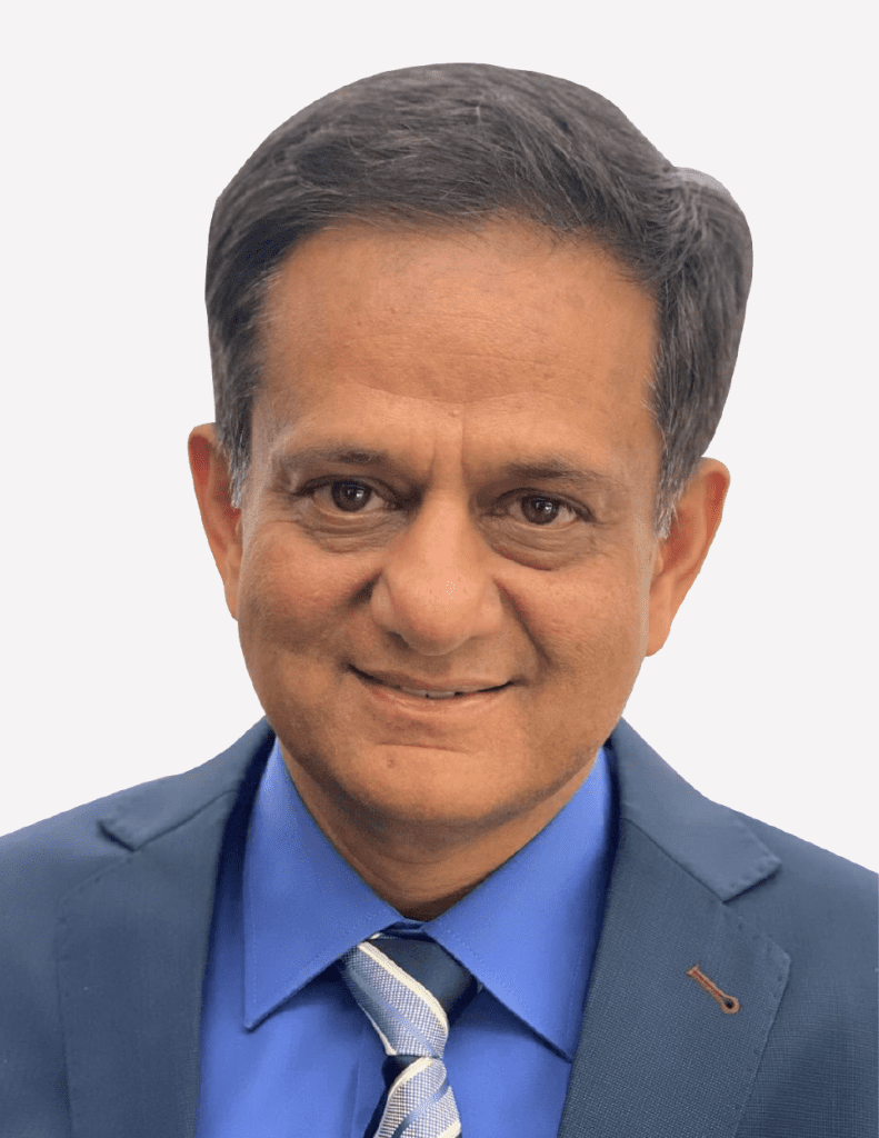 A professional portrait of Sanjay Shah, with a friendly demeanor, wearing a blue suit and a patterned tie, against a plain background.