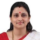 A portrait of a woman with shoulder-length black hair, wearing a red and white saree and a red bindi on her forehead, looking directly at the camera with a neutral expression.