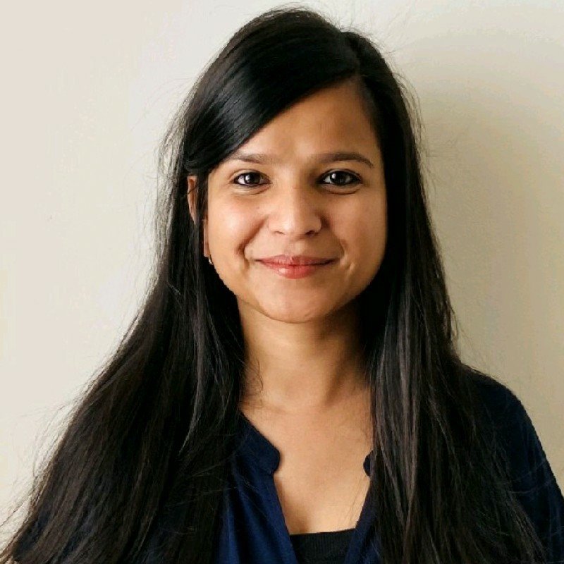A woman with long, straight black hair and a friendly smile is standing against a plain background. She is wearing a dark blue blouse.