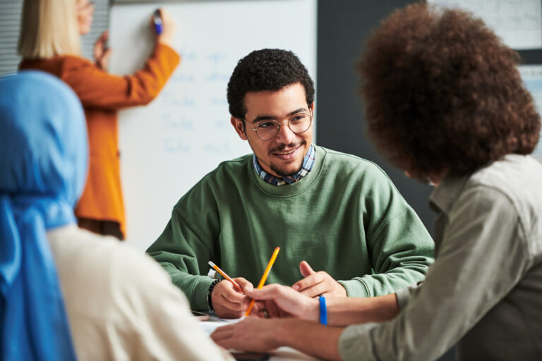 Happy young man in eyeglasses communicating with another student